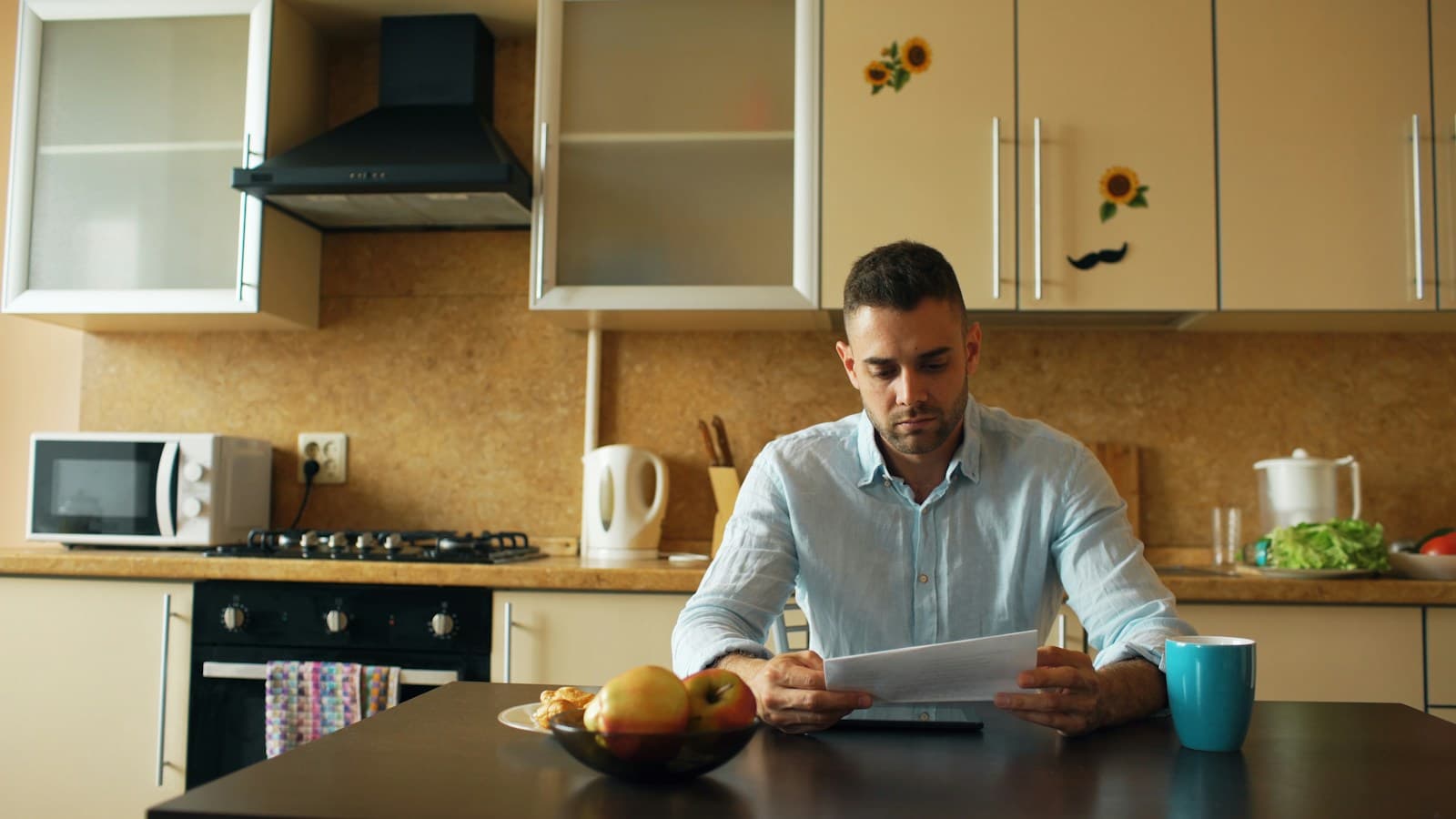 Un homme lit une facture dans sa cuisine, l'air inquiet